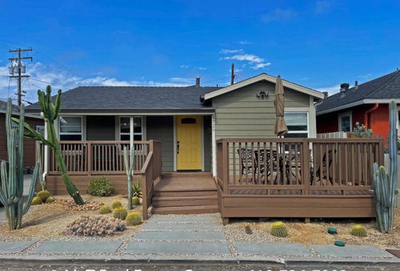 Front exterior of 4728 Works Place in University Heights featuring a yellow door, wooden deck, and drought-tolerant cactus landscaping.