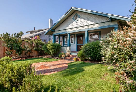 Charming Craftsman bungalow exterior featuring light blue siding, a circular brick paver patio, a green lawn, and a covered porch at 4626 Alabama Street in University Heights.