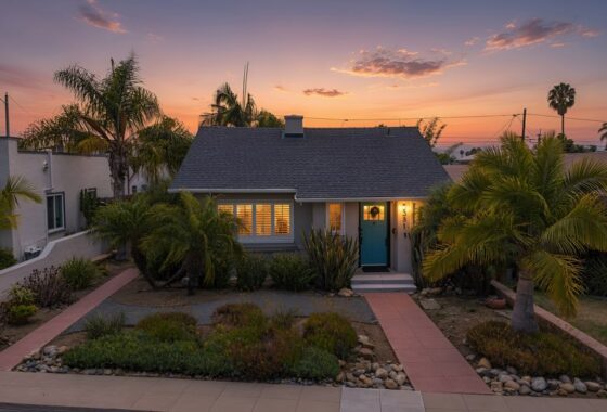 Single-story bungalow home with a grey exterior, turquoise front door, tile walkway, and tropical landscaping at sunset at 3381 Bancroft St in North Park.