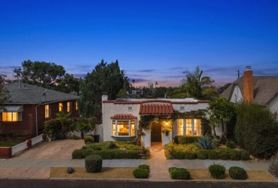 Dusk front exterior view of the Spanish-style single-story house with illuminated windows and a terracotta tile roof at 3568 Villa Terrace in North Park.