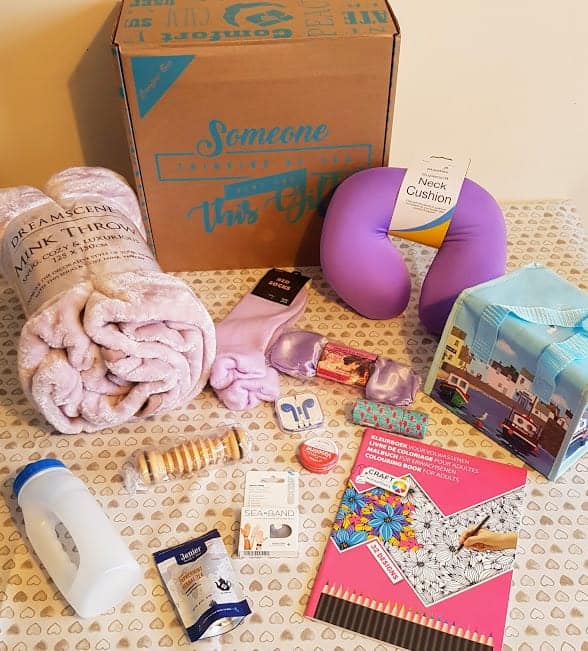 A box with the contents of the cancer care parcel spread on a table with a cream tablecloth covered in hearts.