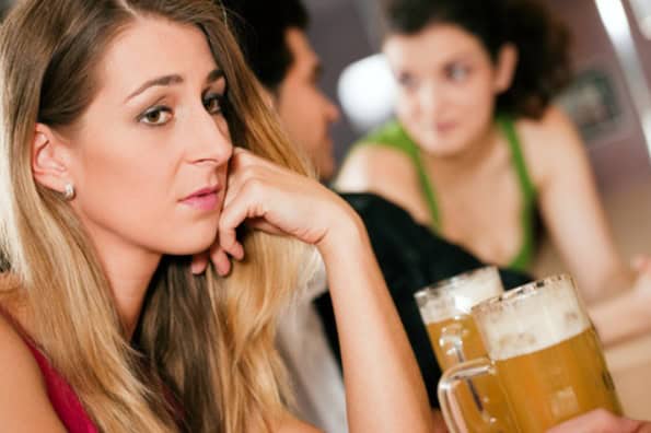Close-up of a lonely woman at the bar who is sad about being single during the holidays while her friends flirt in the background.
