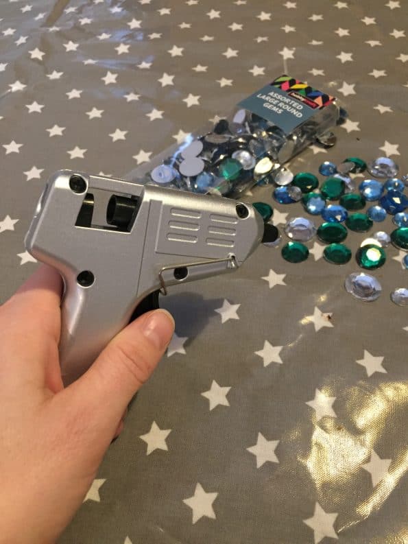 glue gun being held with gems on the table behind