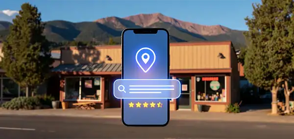 Photorealistic photograph, editorial style. A warm, inviting small business storefront on a sunny Colorado Springs street, with Pikes Peak visible in the background against a bright blue sky. In the foreground, a modern smartphone displays a glowing AI chat interface with a location pin and star rating visible on screen — suggesting an AI search result recommending the business. Natural Colorado light, crisp mountain air feel. No people. No text visible on storefronts or screens. Color palette leans warm and authentic — golden light, blue sky, green mountain tones. Shot as if by a professional commercial photographer. Shallow depth of field with the phone sharp in the foreground and the storefront softly in focus behind it. - What Is GEO — And Why Colorado Springs Businesses Need It Now