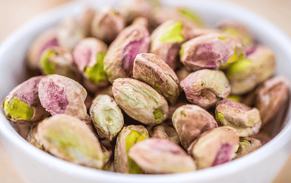 An overhead image of a white bowl with pistachios