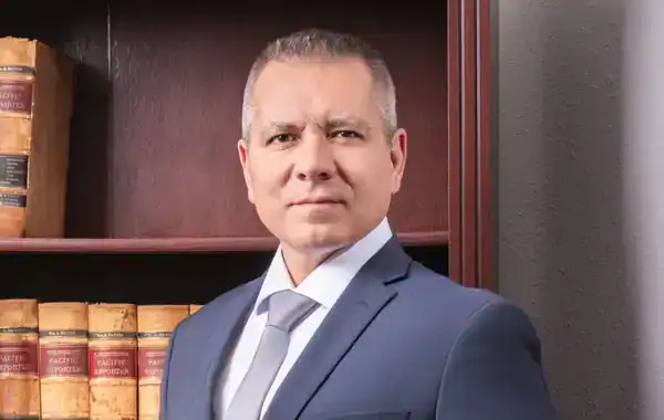 A headshot of Marc A. Grano in a grey suit and grey tie standing in front of a shelf of law books.