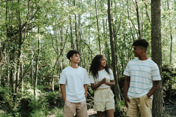 three teenagers on walk in green forest on sunny day