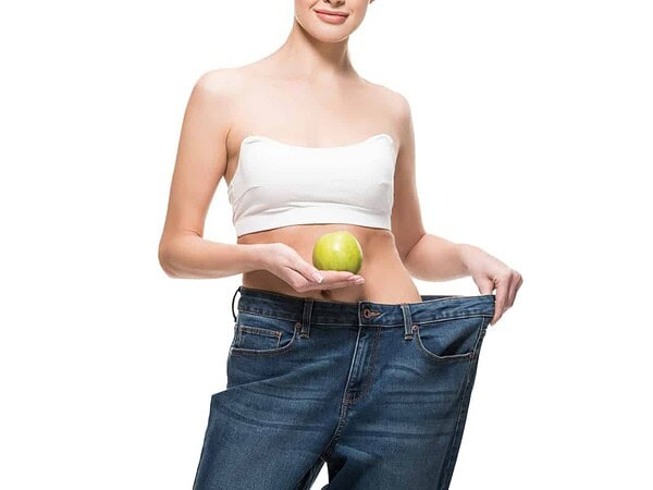 Lady holding large jeans away from her slim body with an apple in her hand on the Slimming world SP plan