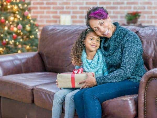 mixed race lady and her daughter cuddling with a gift on the sofa.