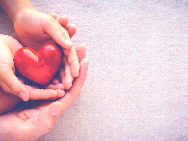 Two pairs of hands holding a red heart