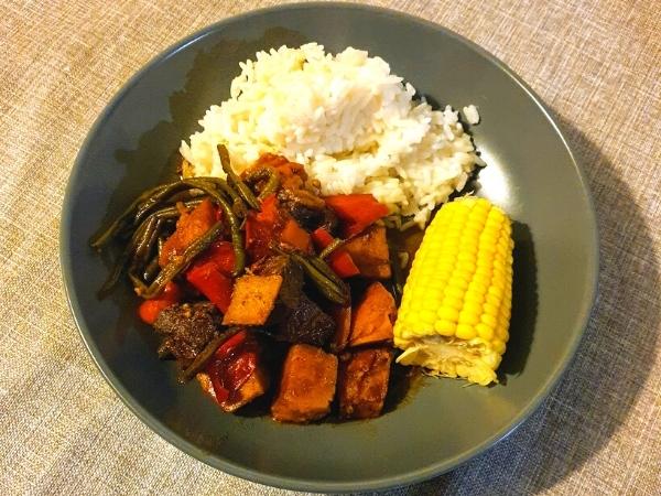 Caribbean pepperpot stew in a grey bowl with rice and a corn on the cob