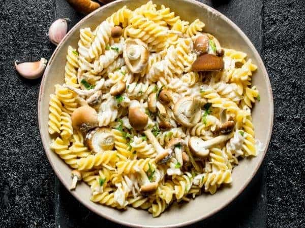 Slimming World garlic mushroom pasta in a beige bowl with a black background 