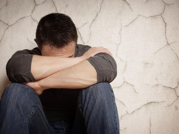 Mental health affecting this man who is sitting on the floor back against a wall with his head in his folded arms