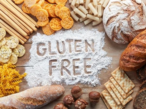 The words gluten free written in flour on a wooden board containing pasta, bread, crackers and various other gluten free foods