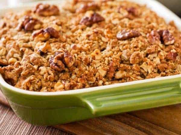 Green casserole dish containing a cooked apple crumble with an oat and walnut topping.