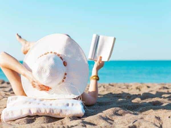 lady reading on the beach in the sun wearing wide brimmed hat