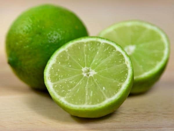 one whole lime and a halved lime on a wooden board