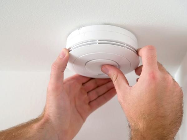 hands testing a smoke alarm on a ceiling