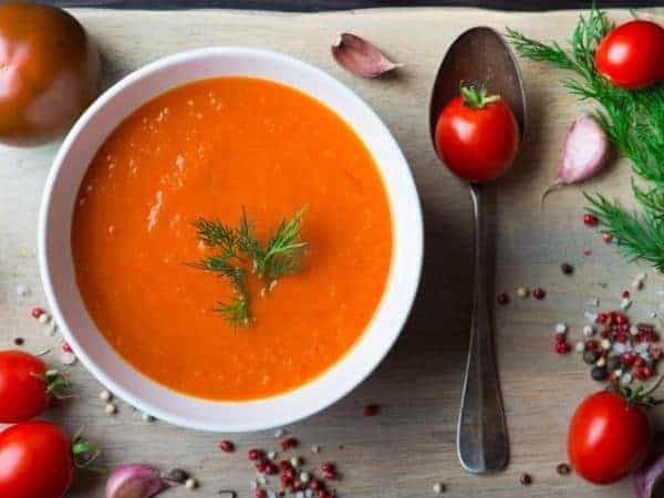 Slimming World tomato soup in a white bowl with spoon and cherry tomatoes