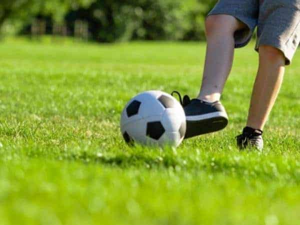 child kicking a football on grass