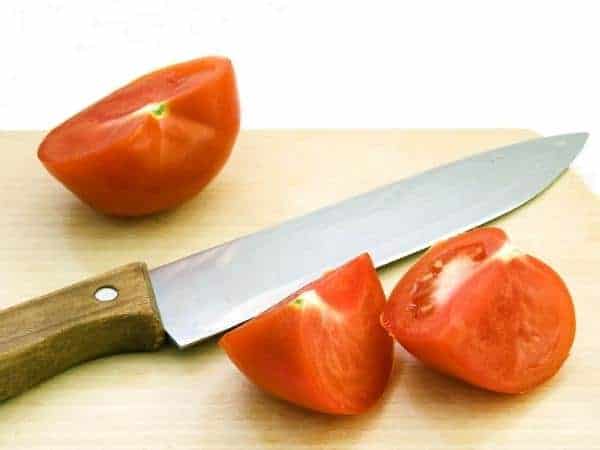 Sharp cutting knife, halved tomatoes on wooden chopping board