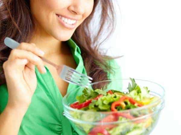 A woman smiling for the camera with a bowl of salad