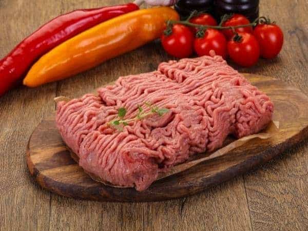 Raw turkey mince on wooden chopping board with vegetables in background ready to cook a Slimming World meal