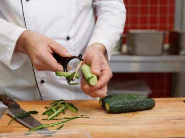 A wooden cutting board, with Cook peeling courgettes