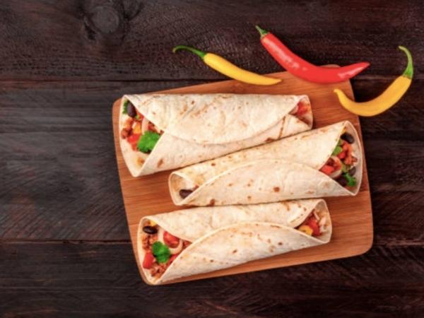 3 Egg and black bean burritos on a wooden board with chillies for decoration