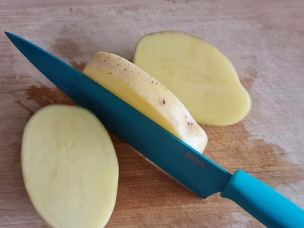 blue knife cutting a potato on a wooden board