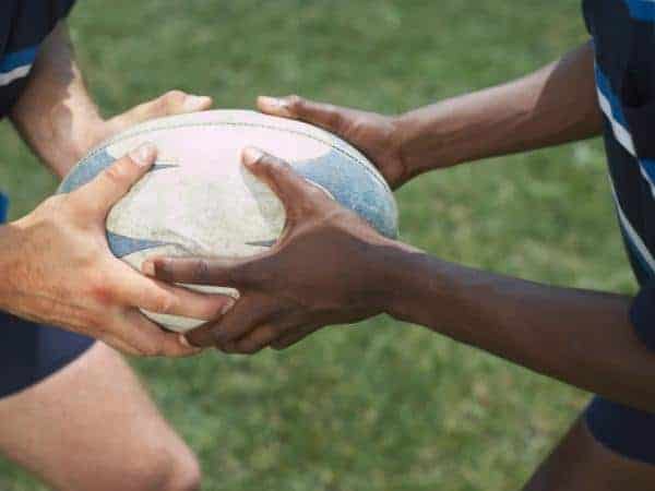 rugby ball being held by two hands white and dark skinned