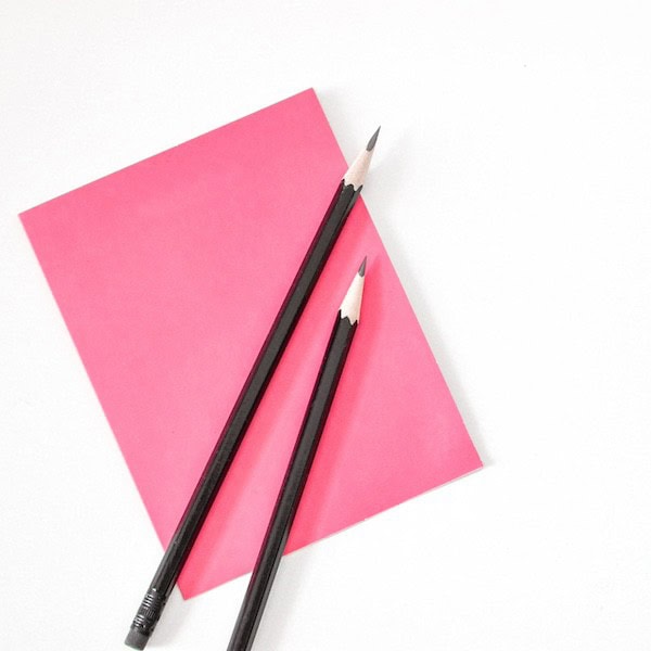 pink note paper with black sharpened pencils angled on top of white desktop
