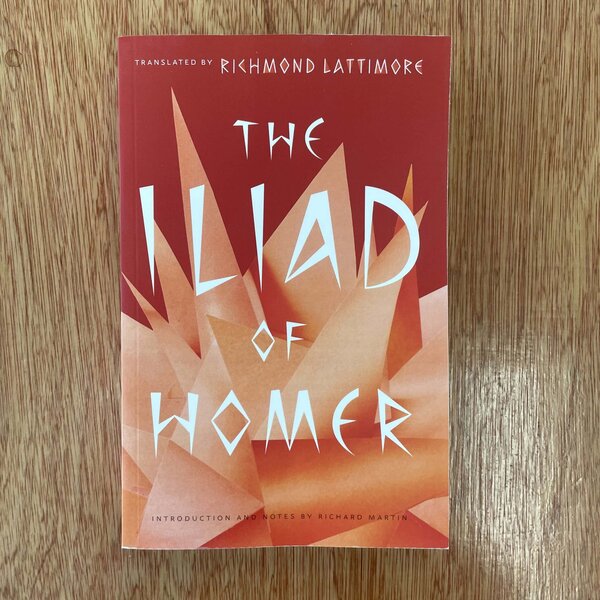 A vibrant red and orange book cover of 'The Island of Wome', translated by Richmond Lattimore, set on a wooden surface, showcasing modern typography and abstract geometric design.