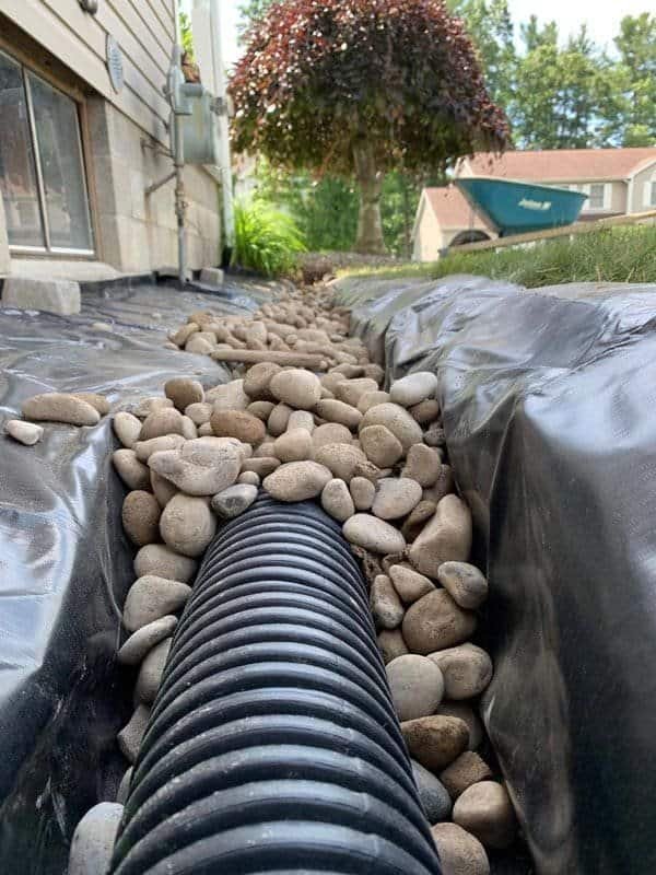 Perforated French drain pipe laid in a fabric-lined trench with river rock in Warren, Oregon