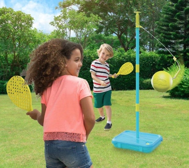 Two children playing hitting a ball attached to a string on a pole outside in the garden.