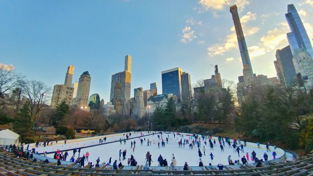 ice skaters at wollman rink with new york city skyline in background