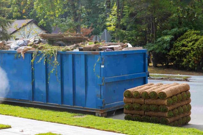 Lawn grass in rolls on pallets against of the street the rolled grass lawn ready for laying and loaded dumpster near construction urban landscape design