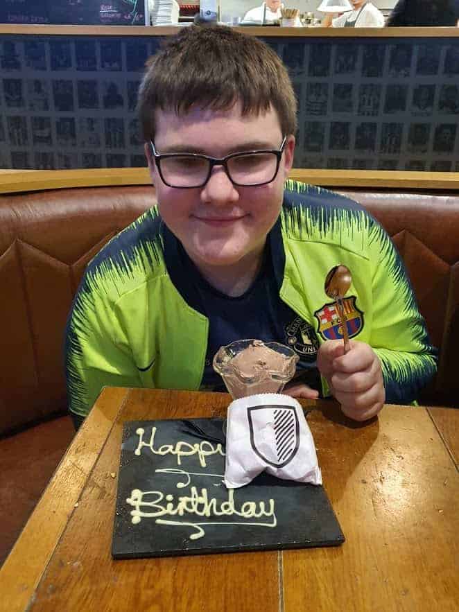 A young boy with glasses posing with his birthday cake