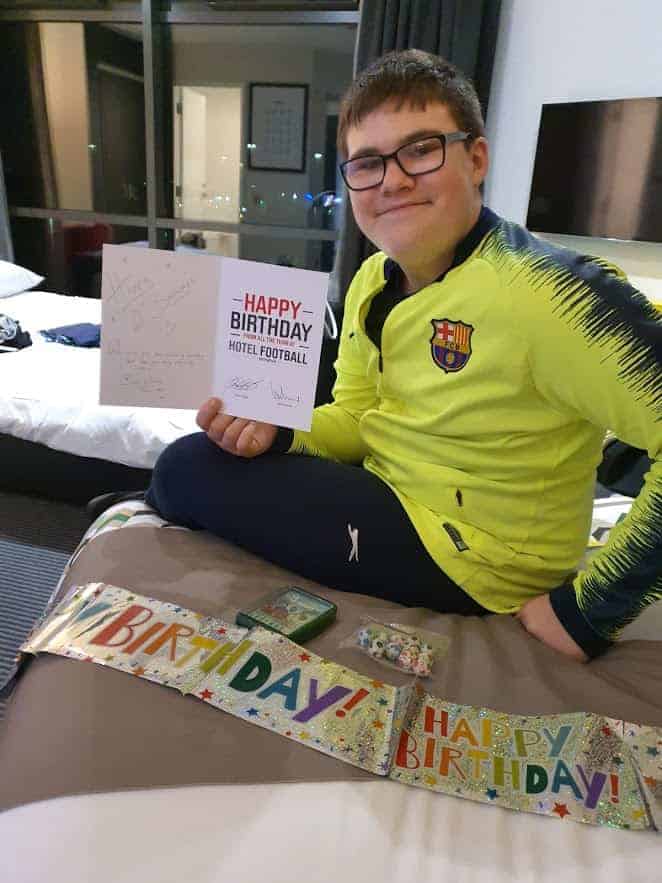 A young boy in yellow shirt holding a happy birthday card with a birthday banner next to him