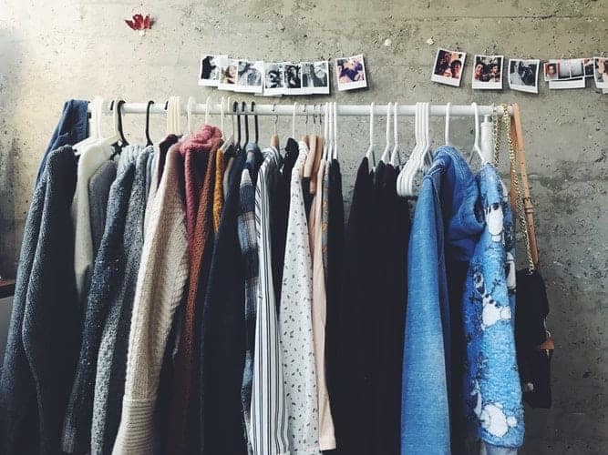 rail of clothes such as cardigans in front of grey wall with poloroid snaps on