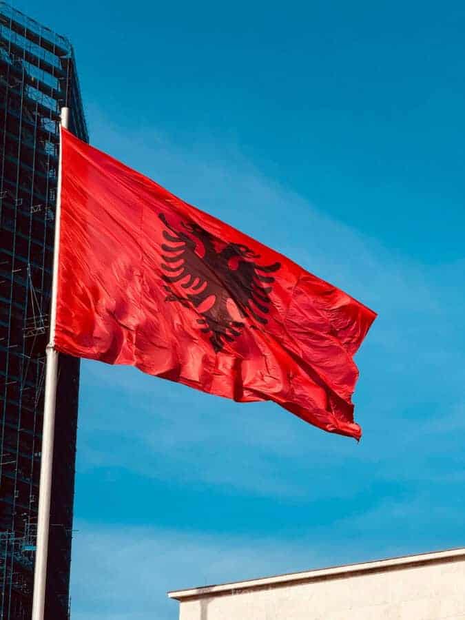 Best Walking Tour of Tirana Route - 5 Must-See Stops. The red Albanian flag flies against a blue sky in Tirana's main square.