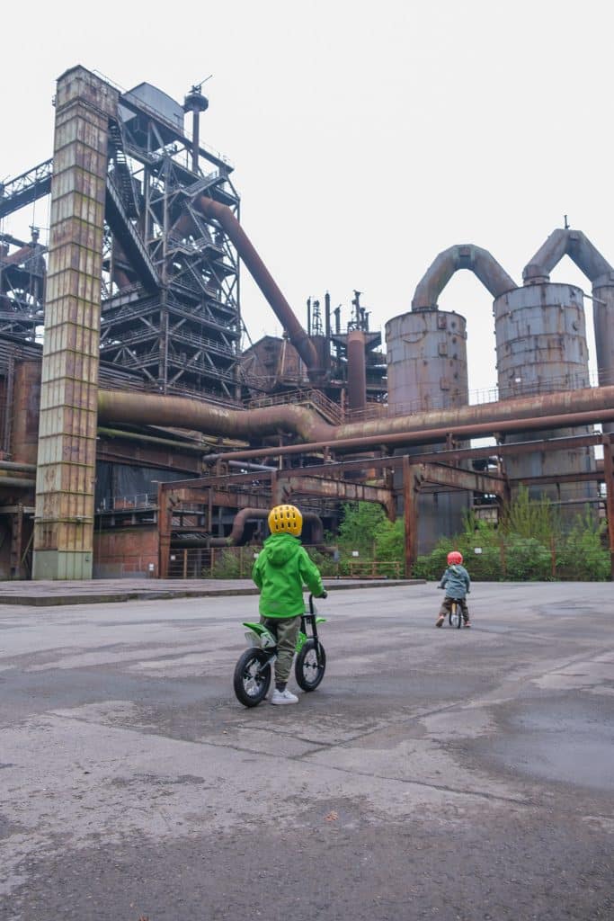 Kinder fahren Laufrad zwischen alten Stahlträgern im Landschaftspark Duisburg-Nord