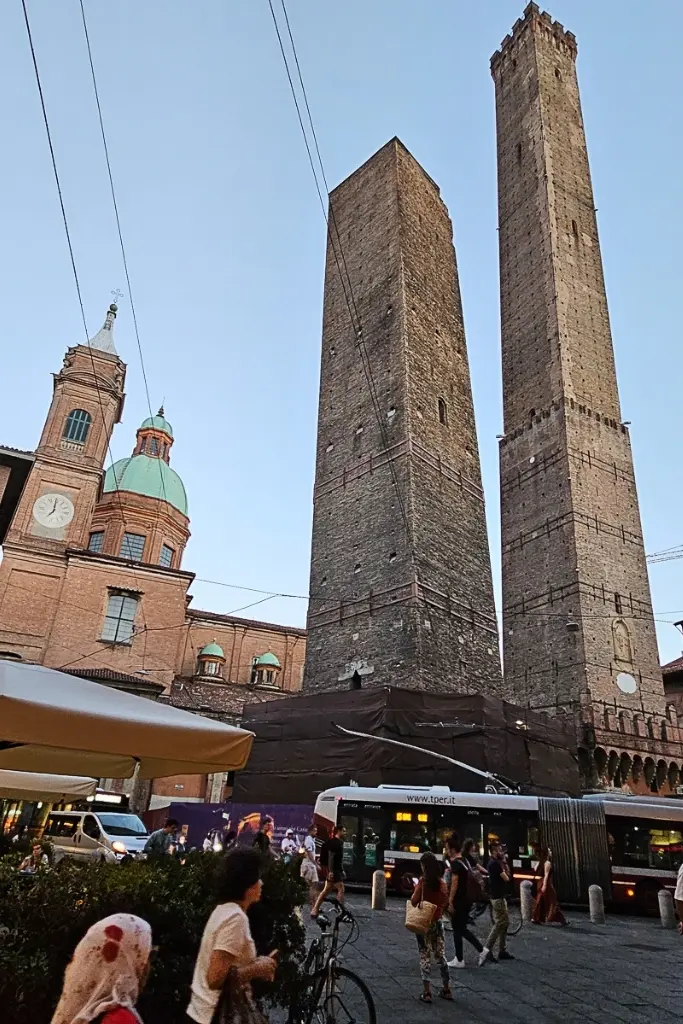View of the Two Towers of Bologna—Torre degli Asinelli and Torre Garisenda—set against a clear sky with bustling street life below, a must-visit landmark and iconic photo stop in Bologna.