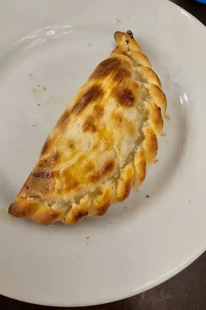 Close-up of a freshly baked Argentine empanada on a white plate — a classic dish you can learn to make in a Buenos Aires cooking class.