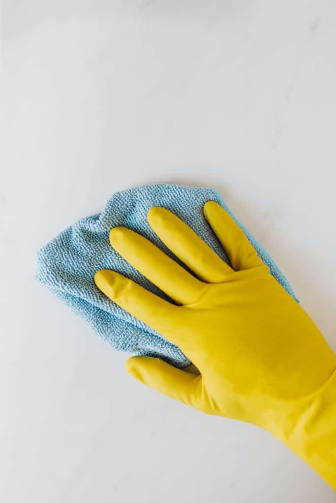 Close-up of a hand in a yellow rubber glove wiping a white surface with a blue microfiber cloth