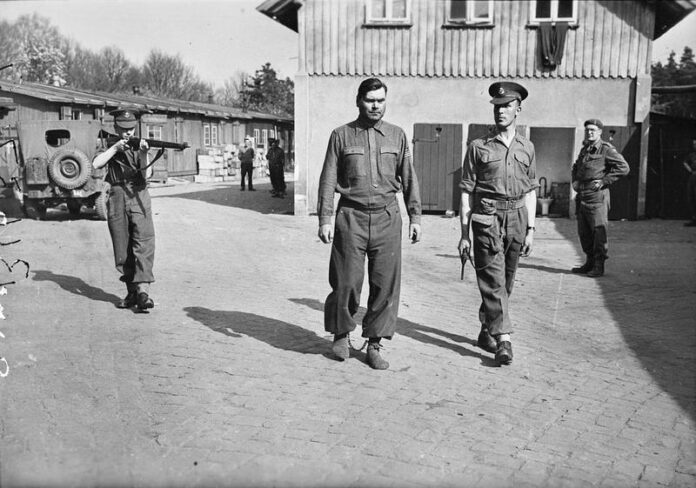 Josef Kramer in boeien na arrestatie, Bergen-Belsen, 17 april 1945. SS-Hauptsturmführer Josef Kramer in boeien, gefotografeerd in Bergen-Belsen voordat hij werd overgebracht naar Celle, 17 april 1945.