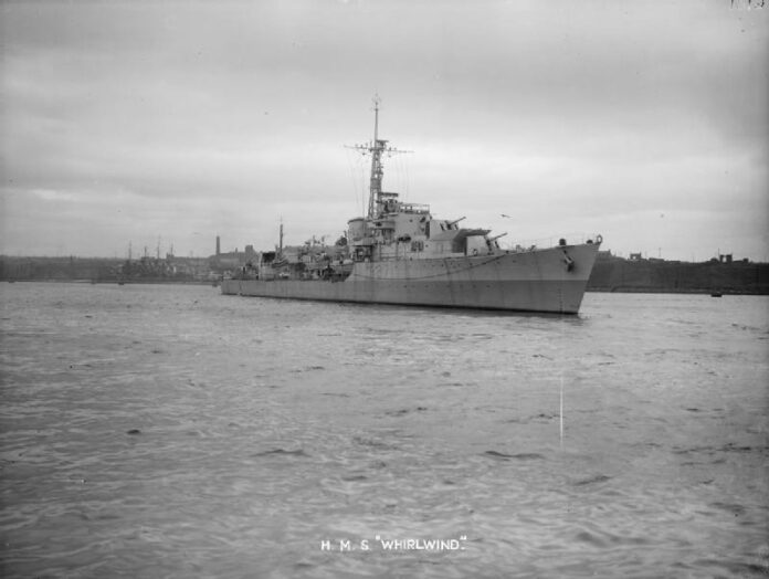 British destroyer HMS Whirlwind sailing near docks, showing wartime configuration with radars and main armament visible.