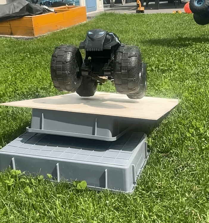 MonsterJAM Megalodon und Batman RC-Autos auf improvisierter Rampe aus Holz und Karton