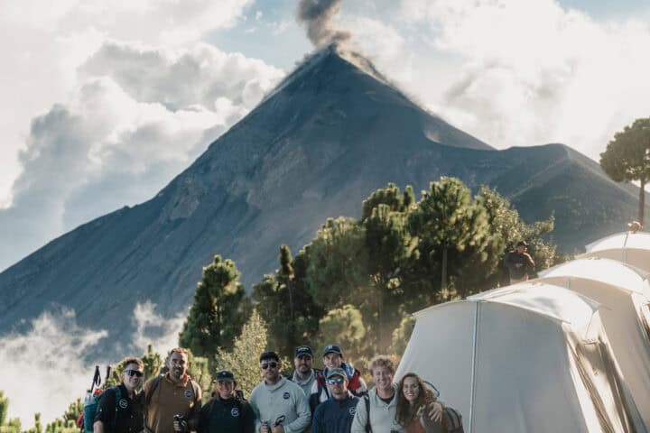 A group of adventurers stands at the OX Expeditions glamping campsite on Acatenango Volcano, Guatemala, with Volcán de Fuego erupting just across the valley. This shot captures the thrill of the Acatenango overnight hike, combining world-class trekking with luxury tents and breathtaking volcanic scenery. Perfect for travelers seeking adventure, photography, and comfort above the clouds.