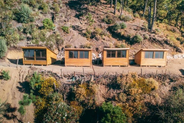 Aerial view of four wooden cabins at OX Expeditions Acatenango campsite lined up against a mountainside